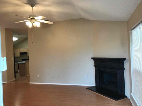 an empty living room with a fireplace and a ceiling fan