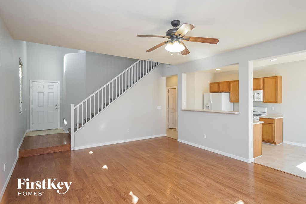 an empty living room with a ceiling fan and a staircase