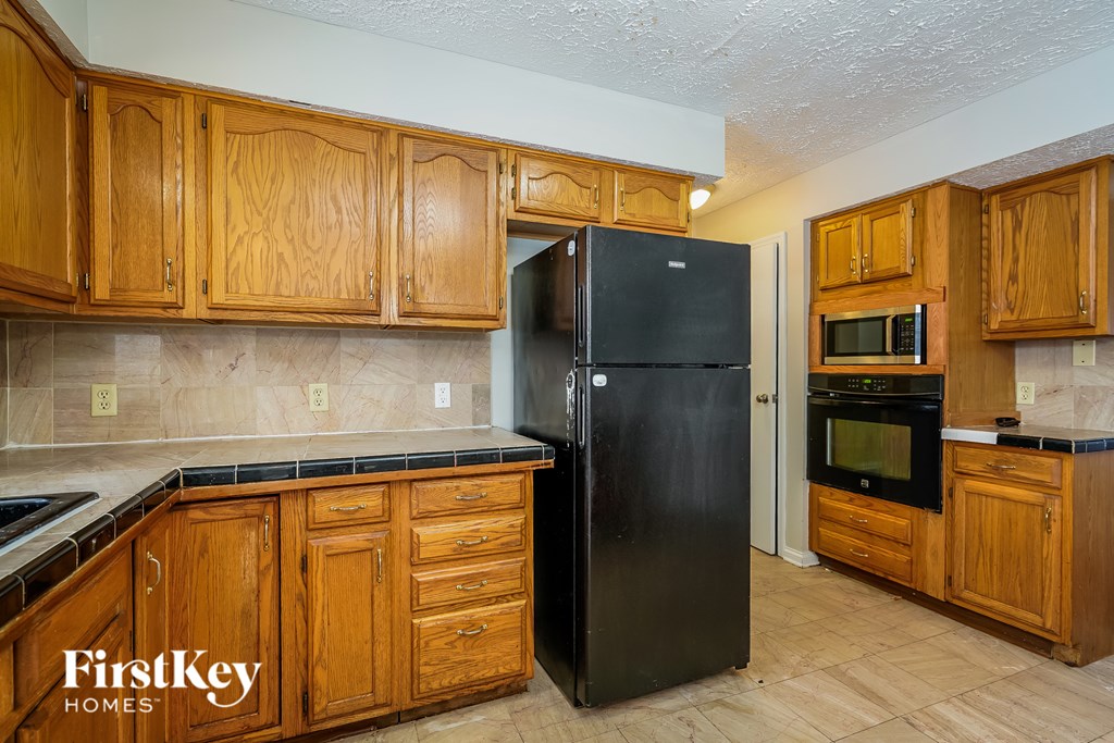 A kitchen with wooden cabinets and a black fridge.