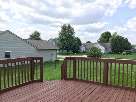 A wooden deck with a railing overlooking a grassy area and houses.