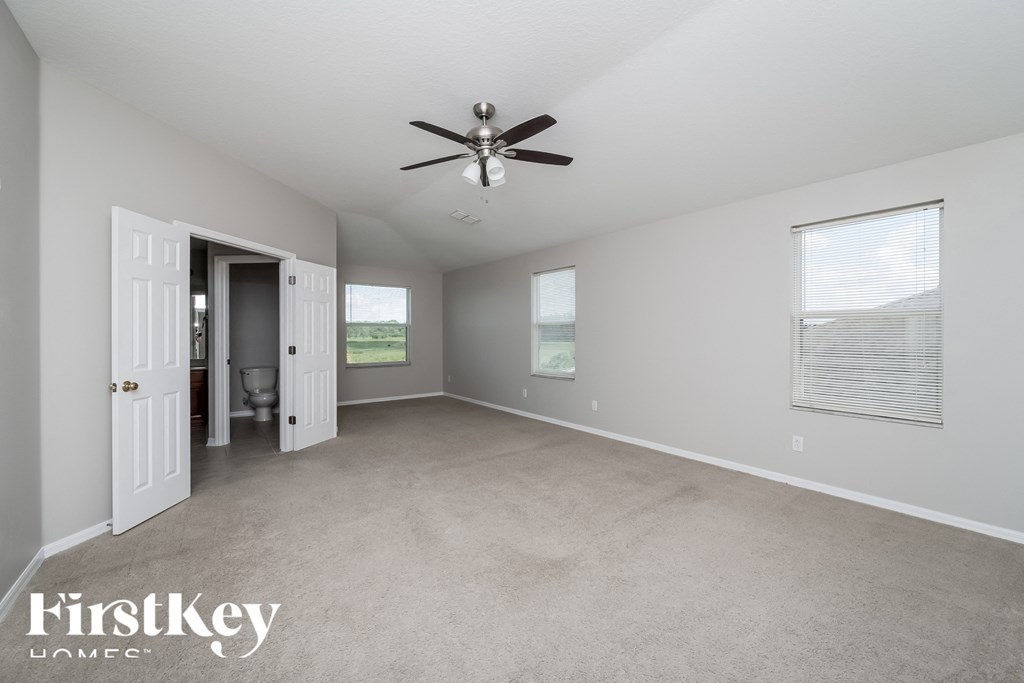 A spacious room with a ceiling fan and two windows.