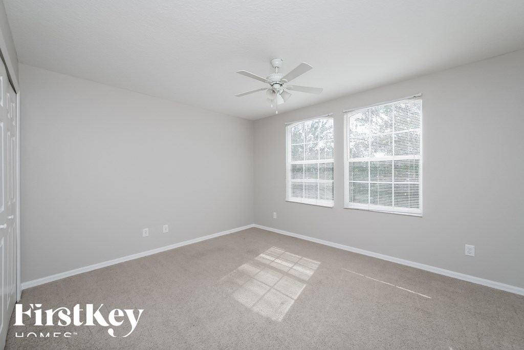 A spacious room with a ceiling fan and two windows.