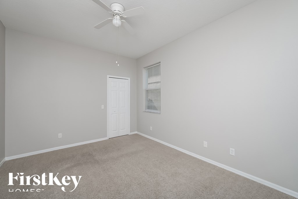 A spacious room with a ceiling fan and a door leading to another room.