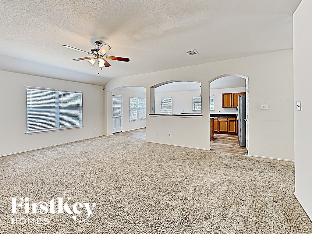 an empty living room with a ceiling fan and a kitchen