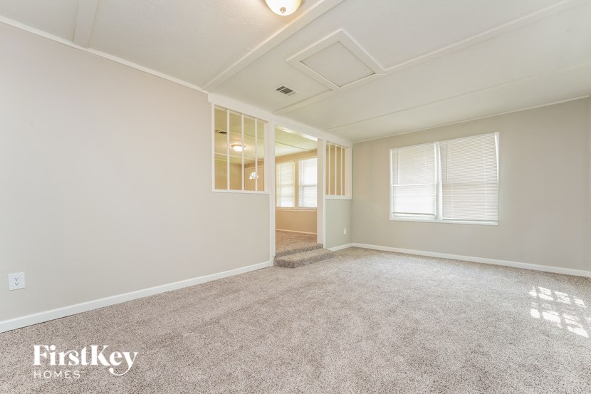 A spacious room with a carpeted floor and a window with blinds.
