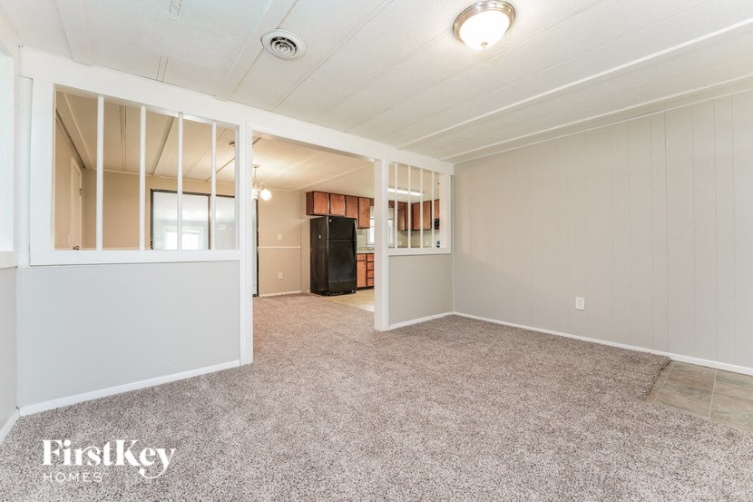 A spacious room with a carpeted floor and a refrigerator in the corner.