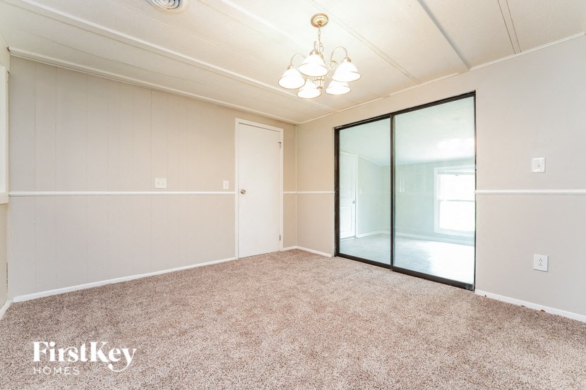 A spacious room with a carpeted floor and a sliding glass door leading to a balcony.