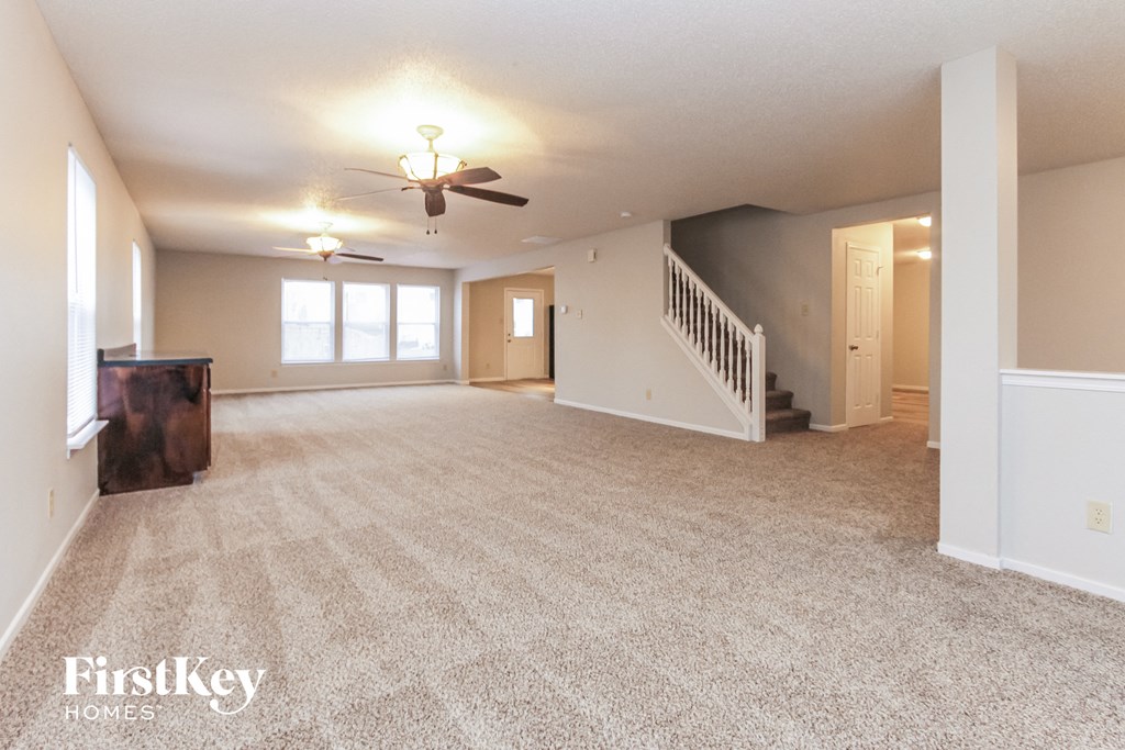 an empty living room with a ceiling fan and a staircase
