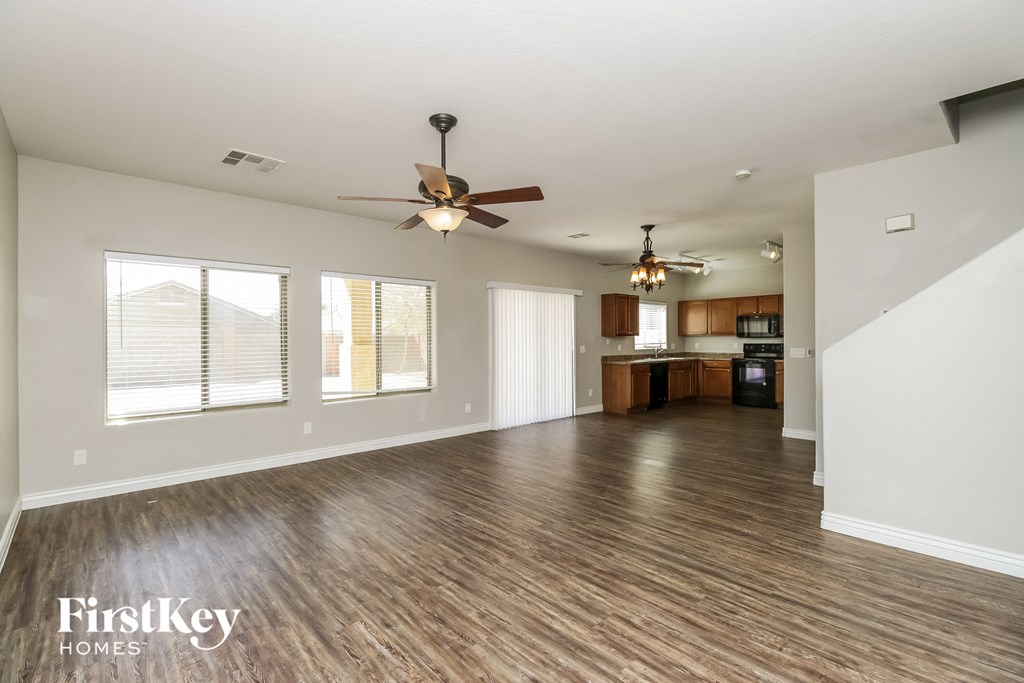 an empty living room with a ceiling fan and a kitchen
