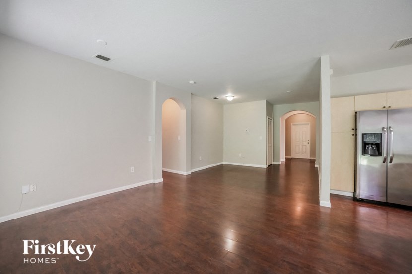 an empty living room with wood floors and a stainless steel refrigerator