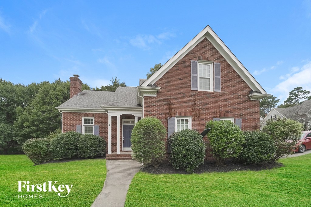 a brick house with a green lawn and shrubs