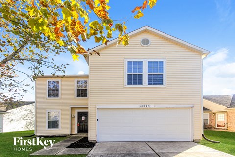 A house with a garage and a tree with yellow leaves in front of it.