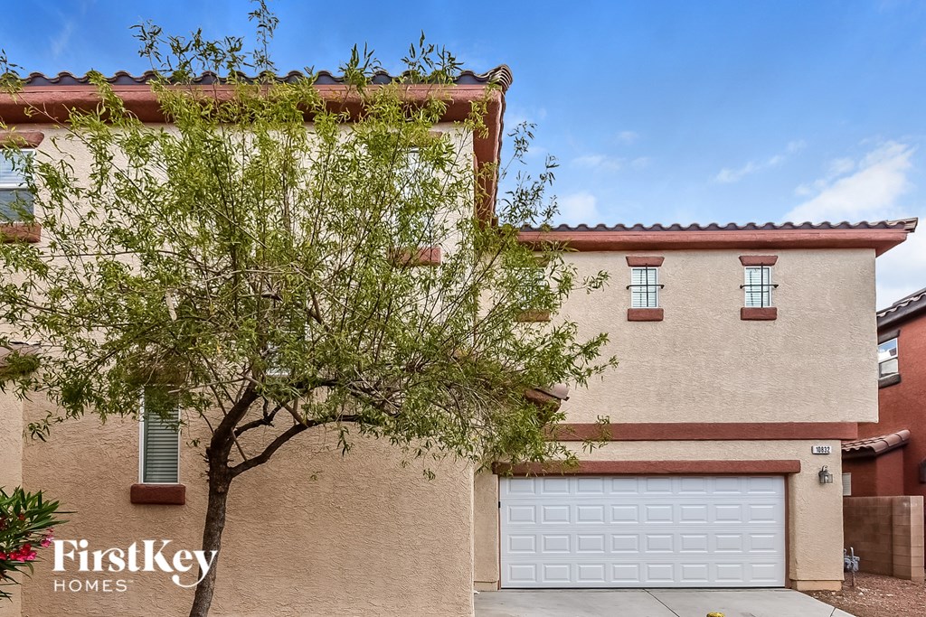 A beige house with a tree in front and a garage door.