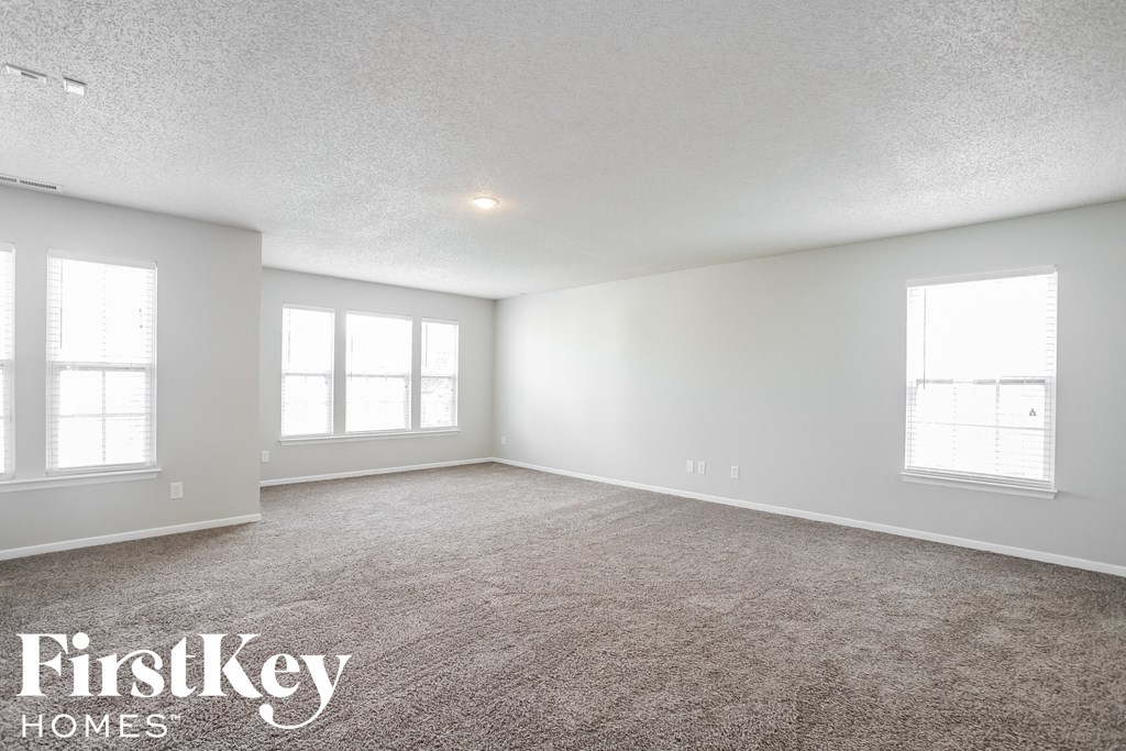 the spacious living room with carpeting and three windows