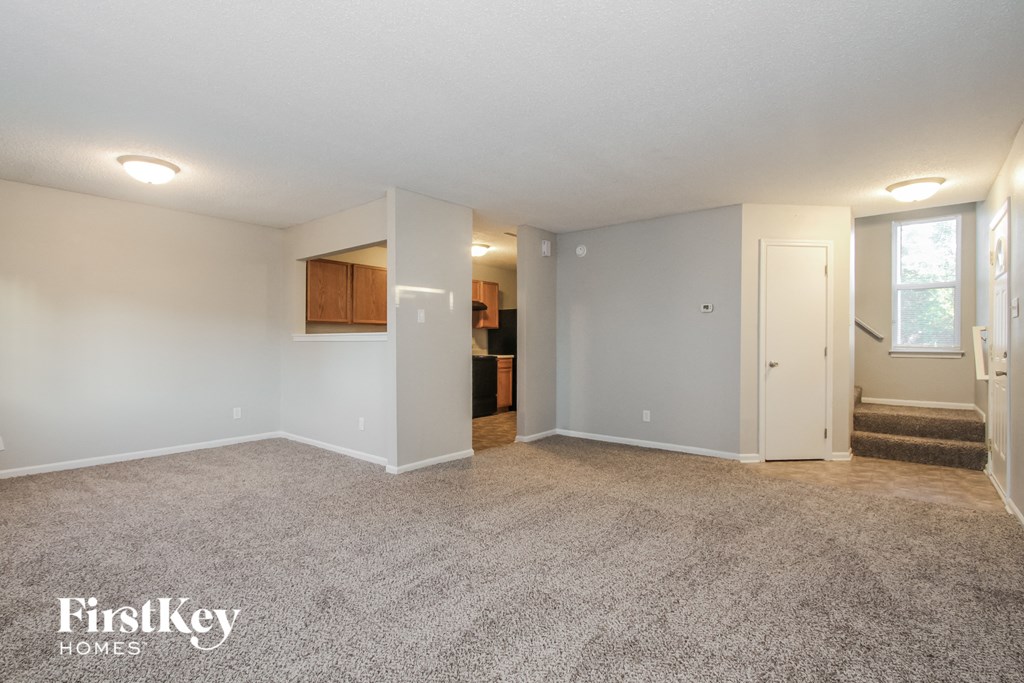 a spacious living room with carpeted flooring and white walls