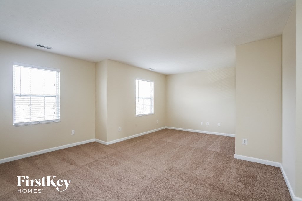 a spacious living room with carpet and two windows