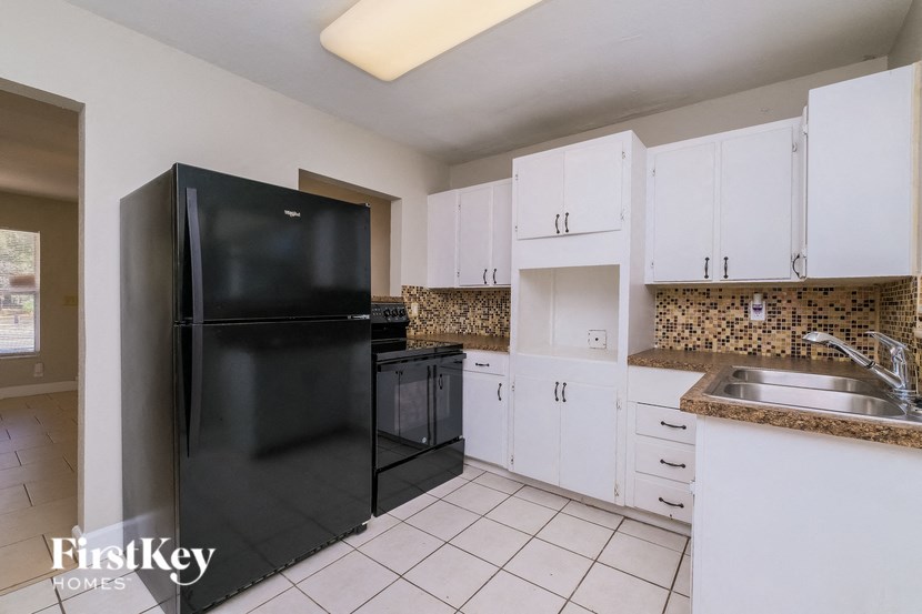 A kitchen with a black fridge and white cabinets.