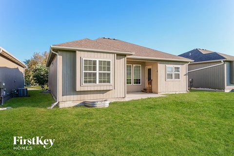 A house with a brown roof and a white door is surrounded by a grassy lawn.