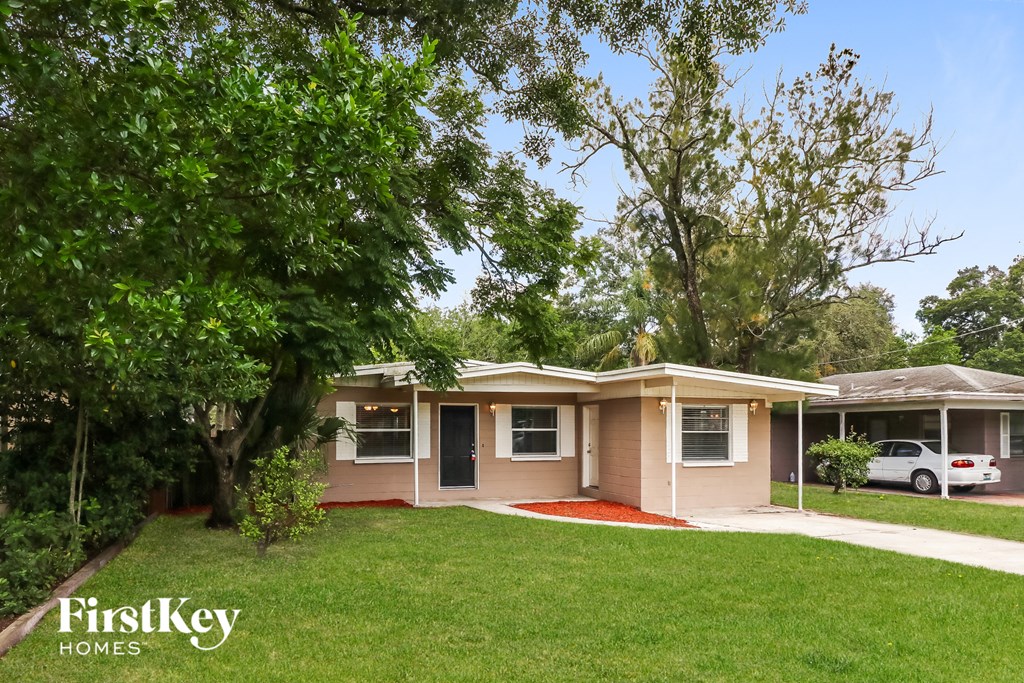 A house with a red carpet is surrounded by greenery and has a tree in front of it.