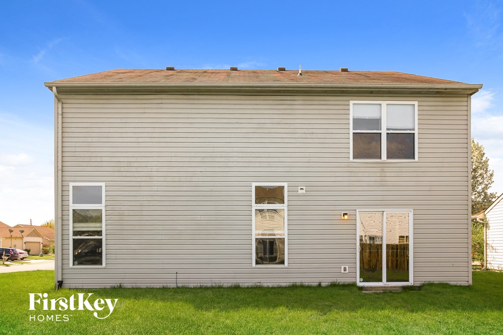 backyard view of the front of a gray house with white siding and grass