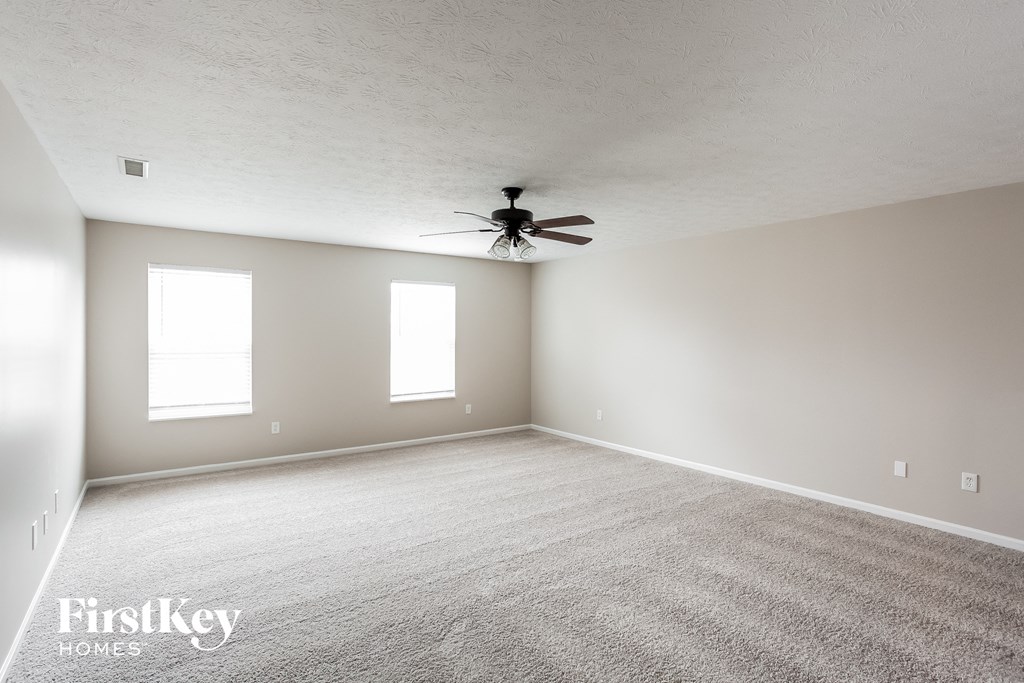 A spacious room with a carpeted floor and a ceiling fan.