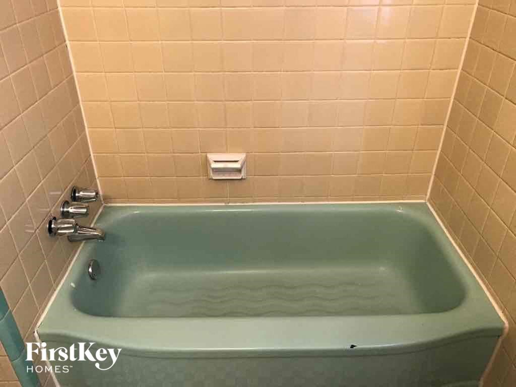 A white tiled bathroom with a green tub and a white faucet.