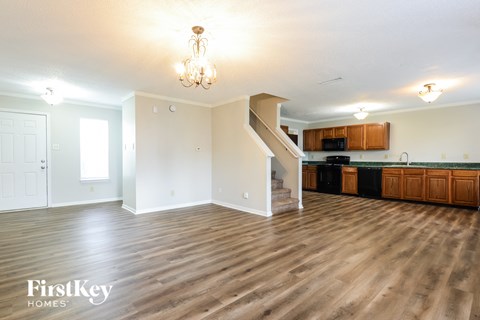 A well-lit, empty living room with wooden floors and a staircase leading to the upper level.