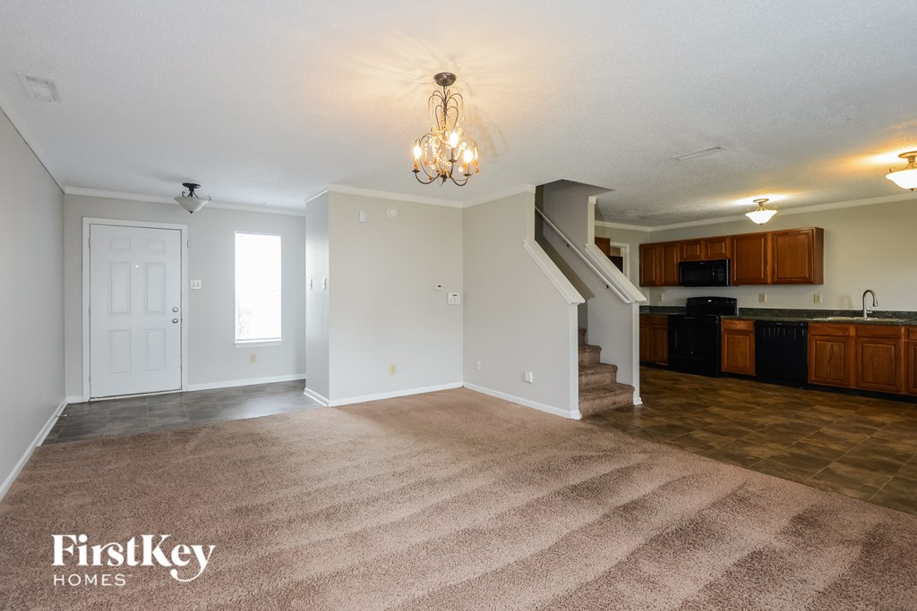A well-lit, empty living room with a staircase leading to the kitchen.