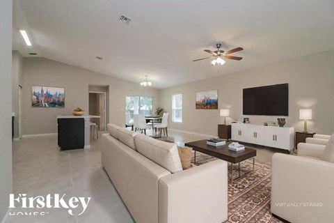 A spacious living room with a white sofa set and a television on the wall.
