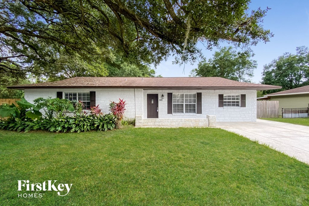 A white house with a brown roof and a green lawn in front.