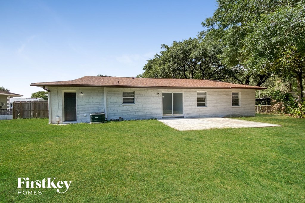 A small house with a brown roof and a white exterior is surrounded by a grassy yard.