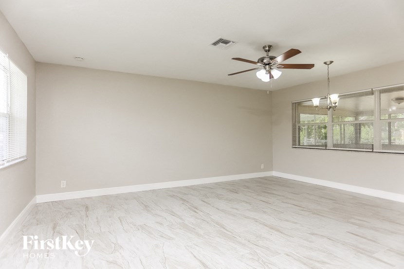 A spacious room with a ceiling fan and light fixture, and a large window with blinds.