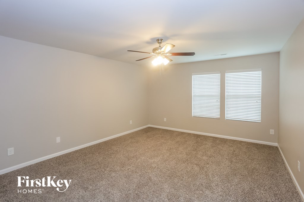A room with a carpet floor, a ceiling fan, and a window with blinds.