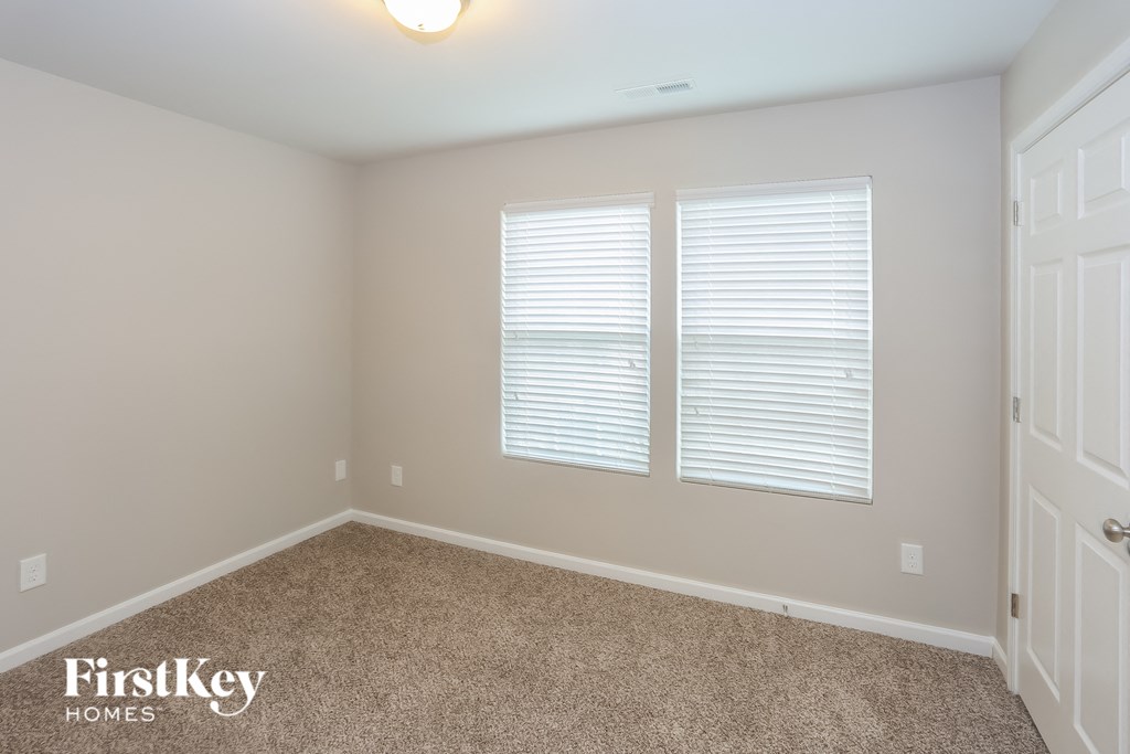 A room with a carpeted floor, a window with blinds, and a door.