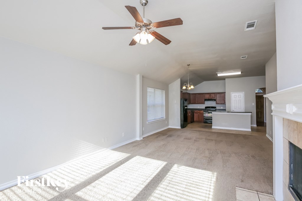 an empty living room with a ceiling fan and a kitchen
