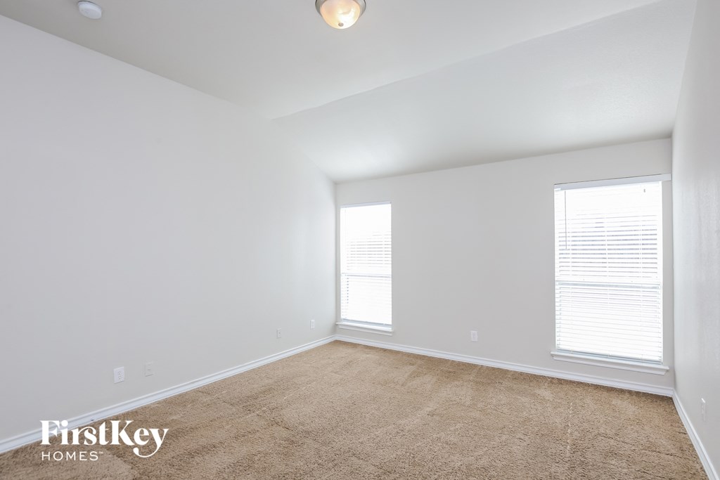 a spacious living room with white walls and carpet and two windows