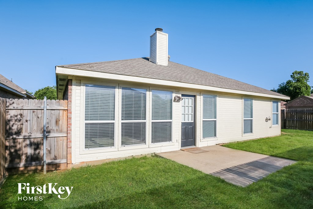 the backyard of a small white house with a yard and a fence