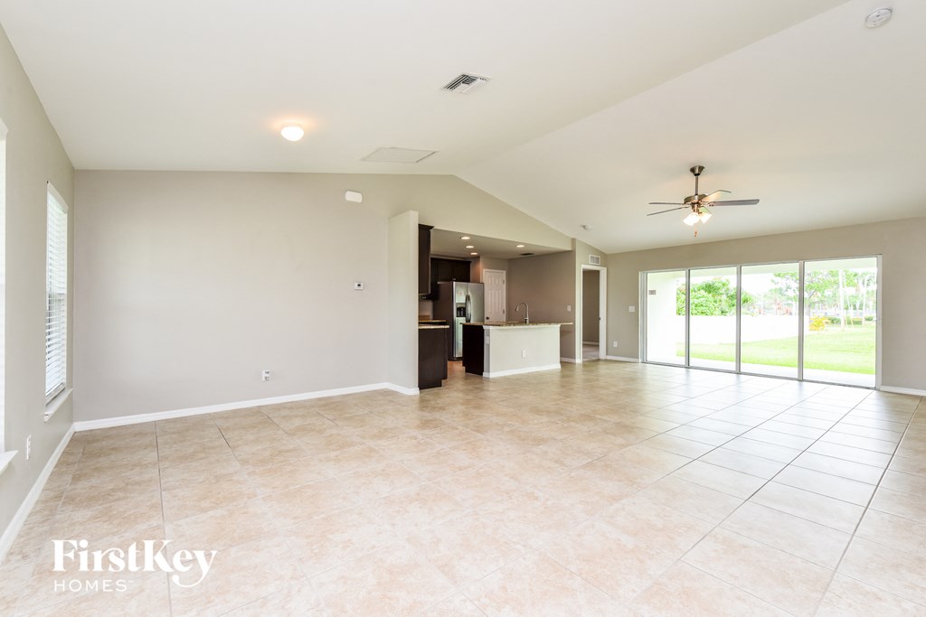 an empty living room with a kitchen and a ceiling fan