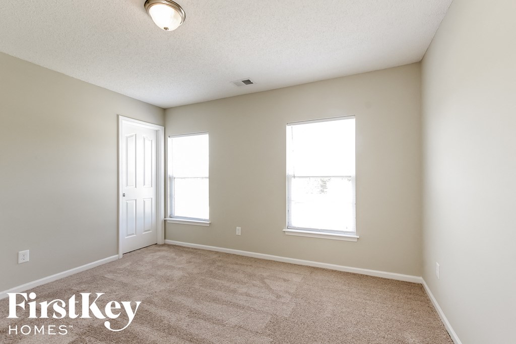 a spacious living room with a carpeted floor and two windows