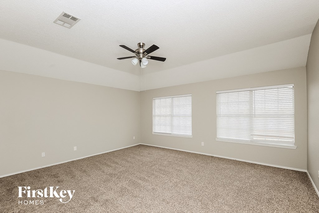 an empty room with a ceiling fan and two windows