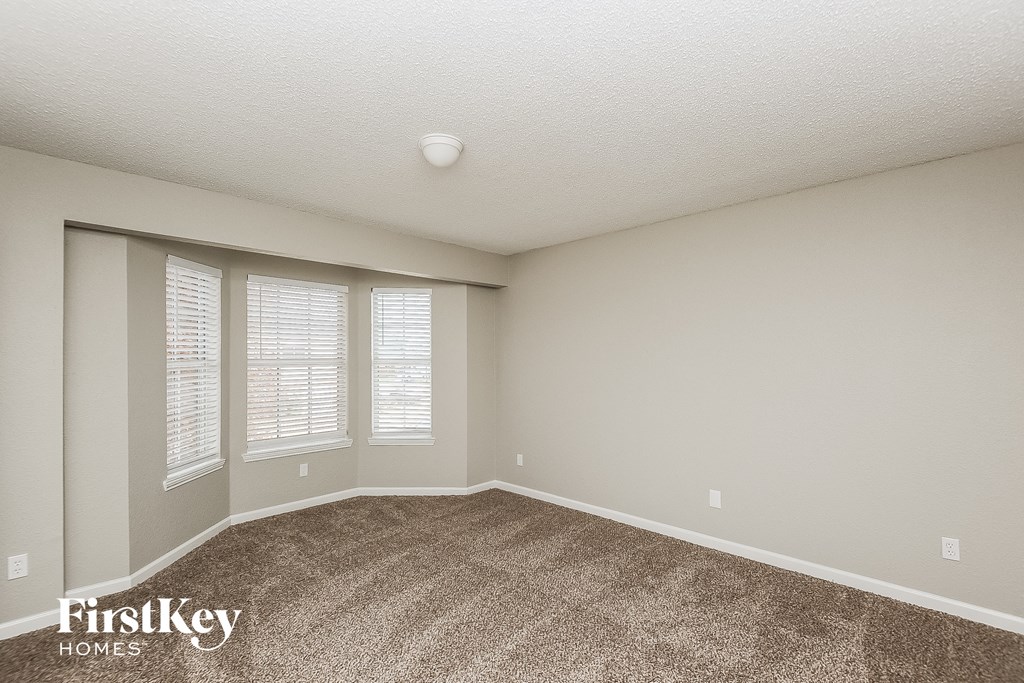 an empty living room with carpet and three windows
