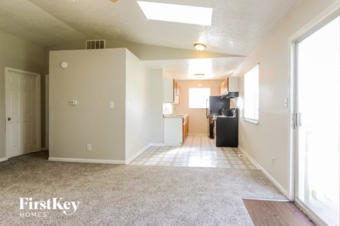 an empty living room with a kitchen in the background