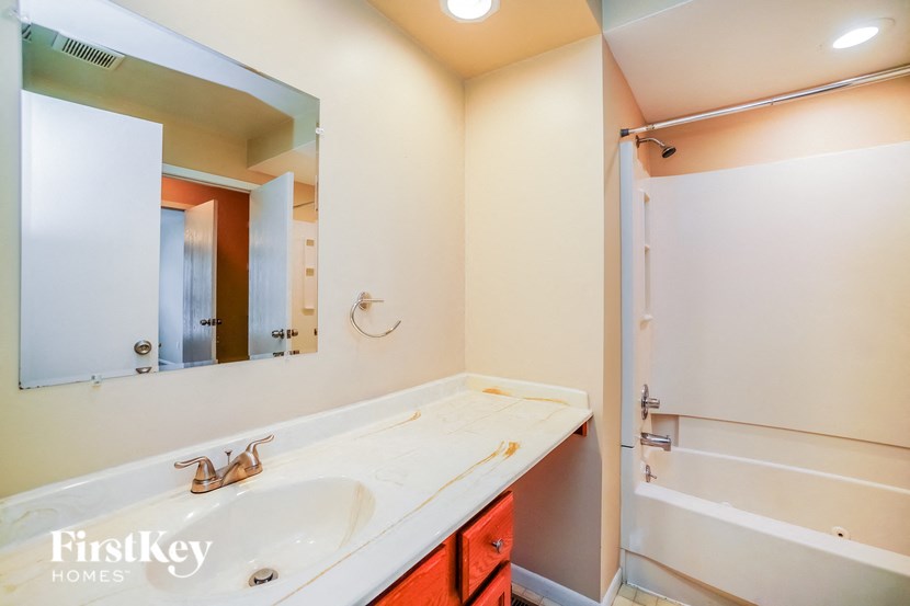 A bathroom with a sink, mirror, and bathtub.