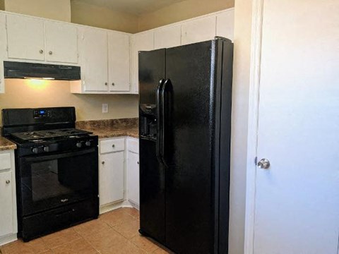 A black refrigerator stands in a kitchen with white cabinets.