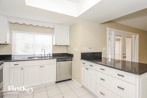 A kitchen with white cabinets and black countertops.