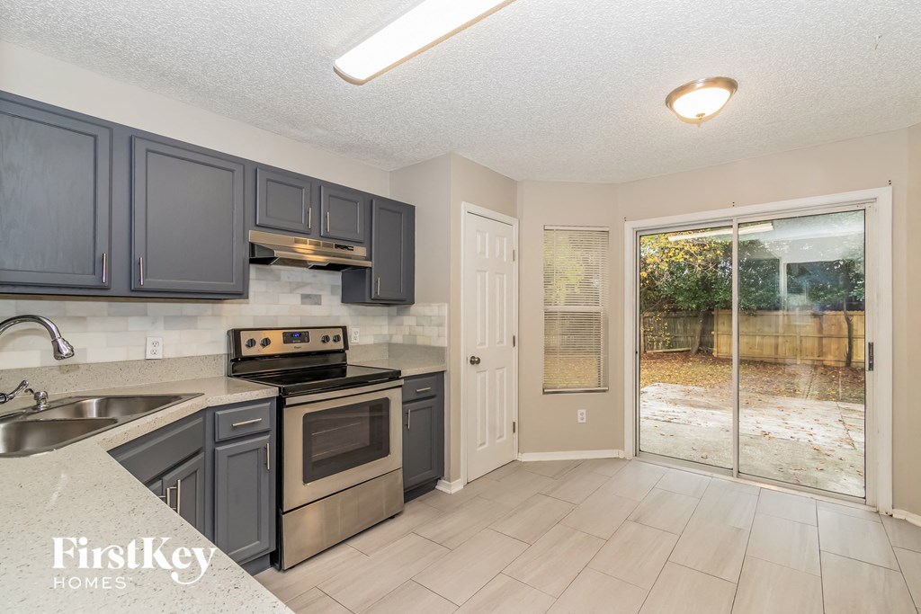a kitchen with gray cabinets and stainless steel appliances and a sliding glass door