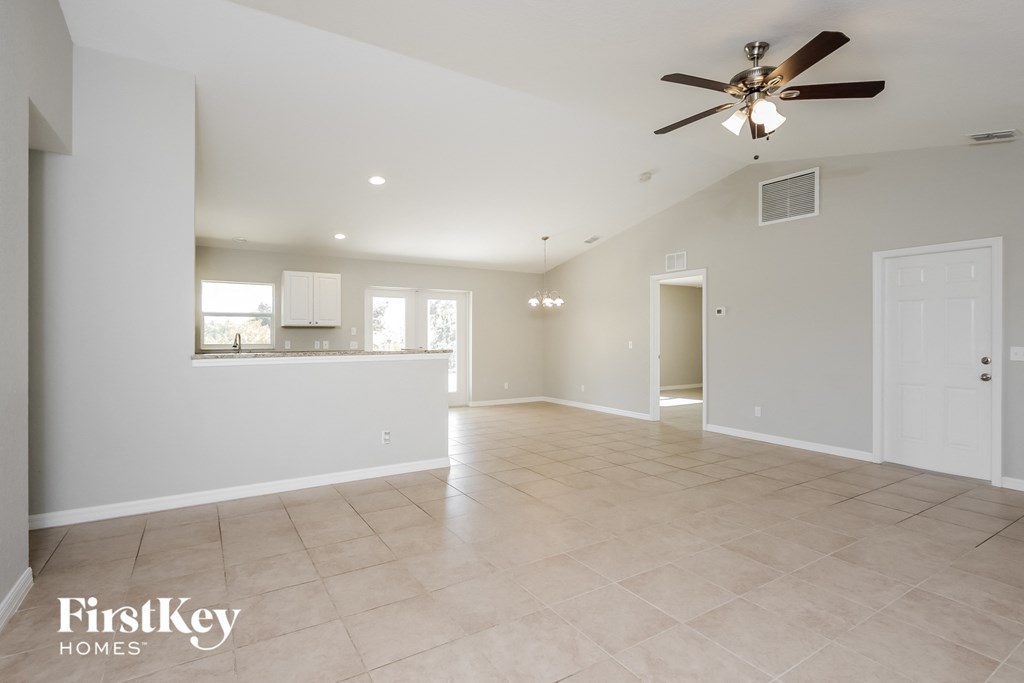 an empty living room with a ceiling fan and a kitchen