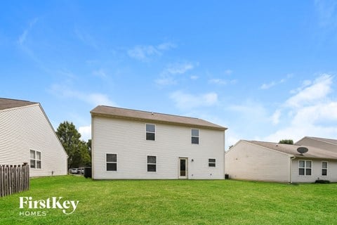 A white house with a black door and windows is in the foreground of a grassy field.