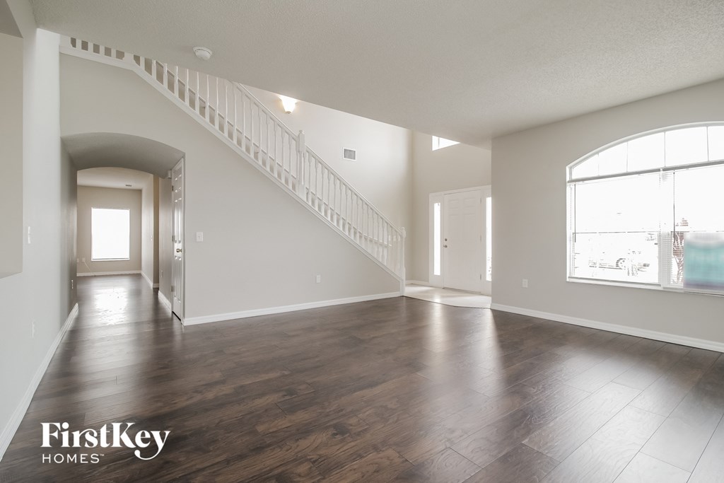 A spacious living room with wooden floors and a staircase leading to the upper level.