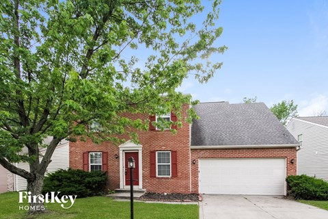 a red brick house with a white garage door and a tree